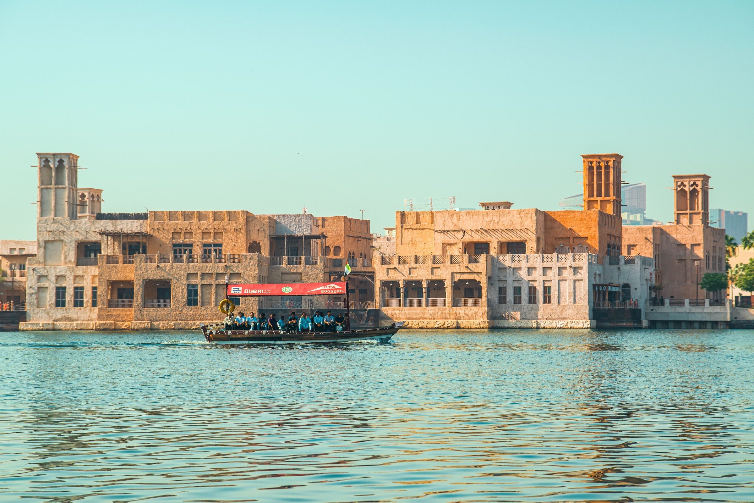 Abra boat sailing along Dubai Creek with traditional architecture in the background during sunset