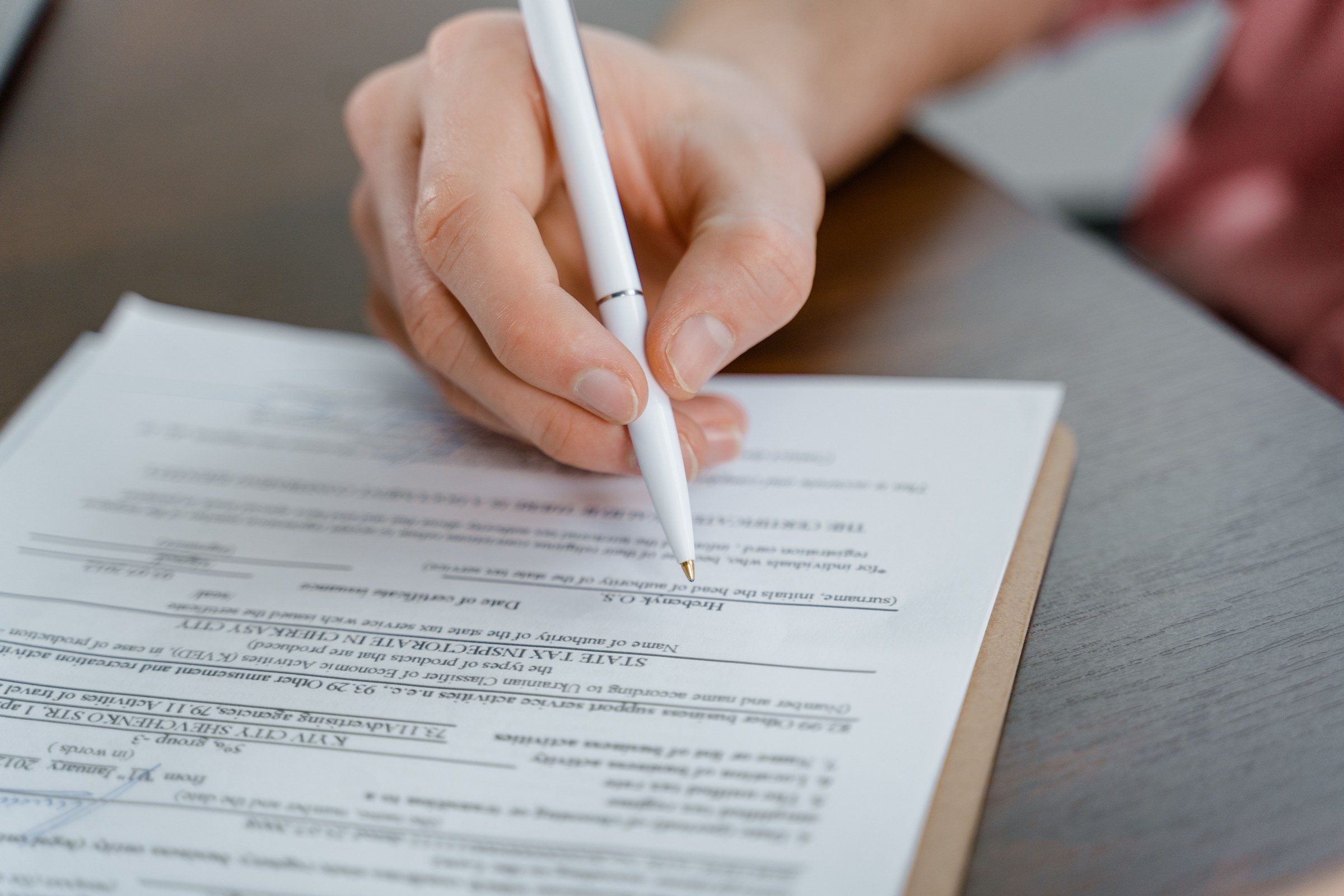A hand holding a pen signing a document, close-up shot with focus on the paper