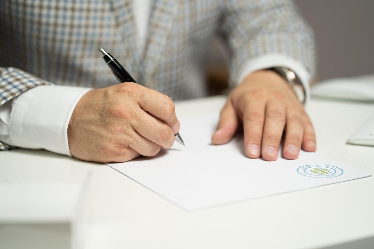 A person signing a document at a white desk, illustrating the legal terms used in the UAE