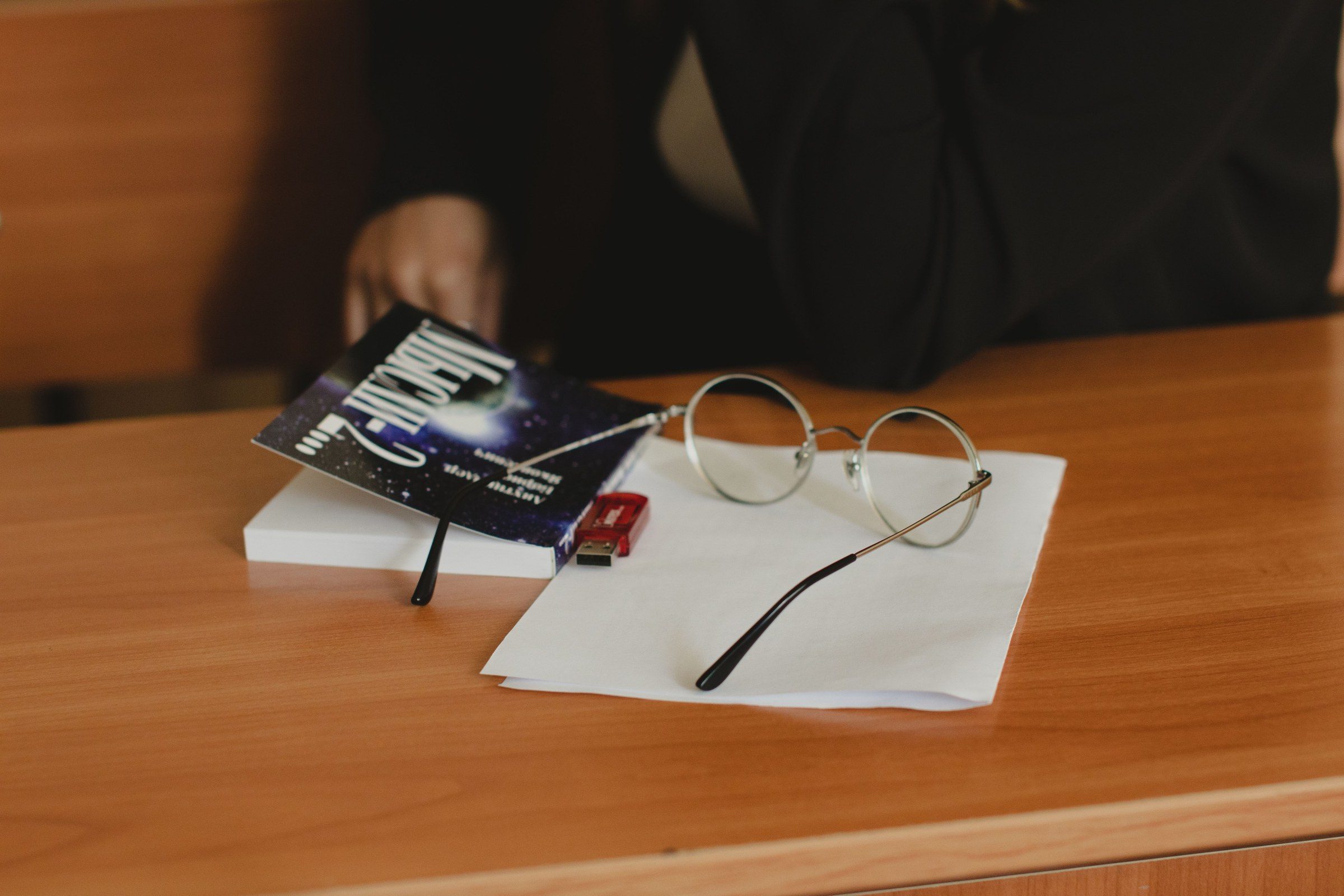 Eyeglasses, a book and a USB drive on a wooden desk, illustrating what a legal consultant is in the UAE