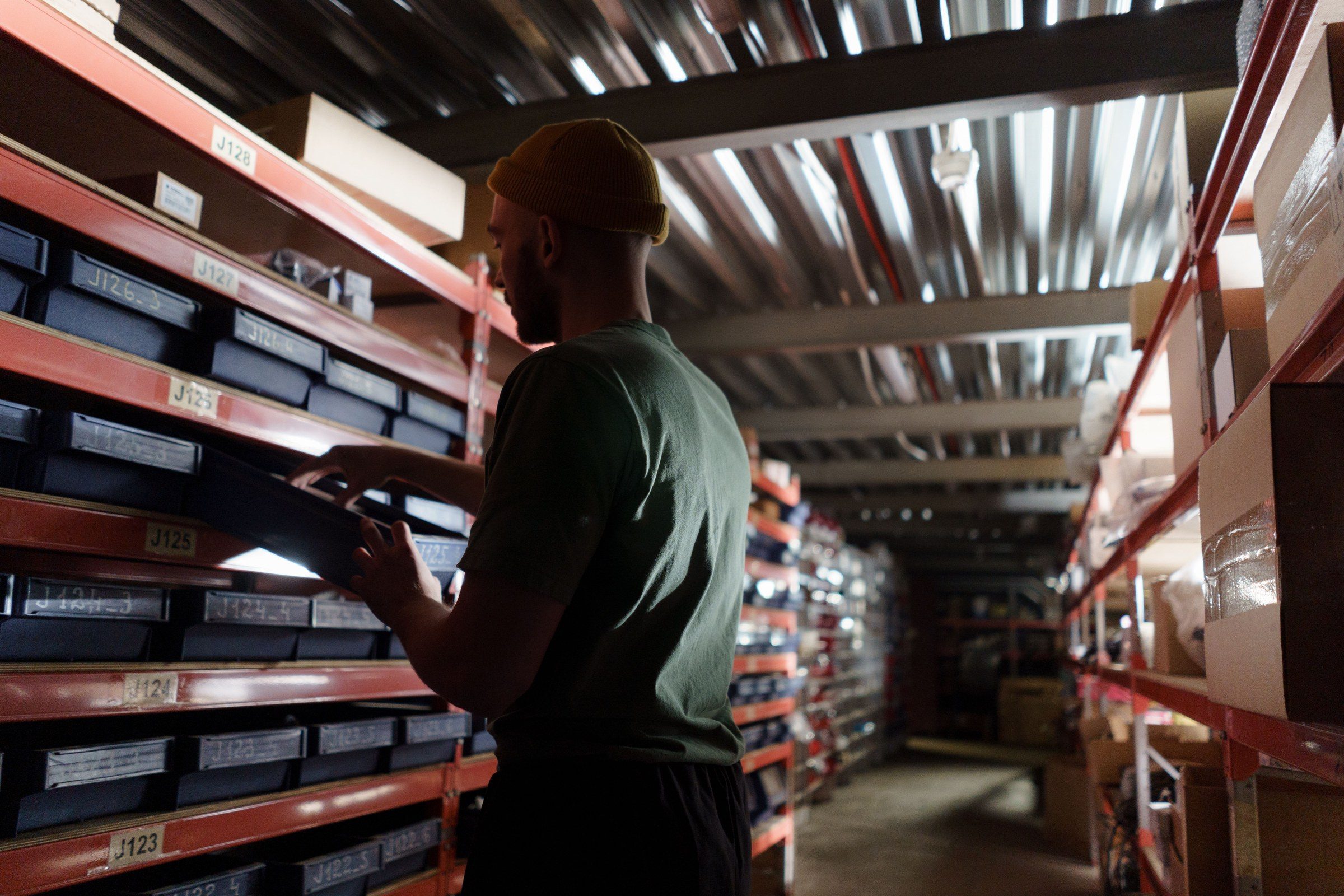 A man organizing inventory on shelves in a dimly lit warehouse, wearing a uniform