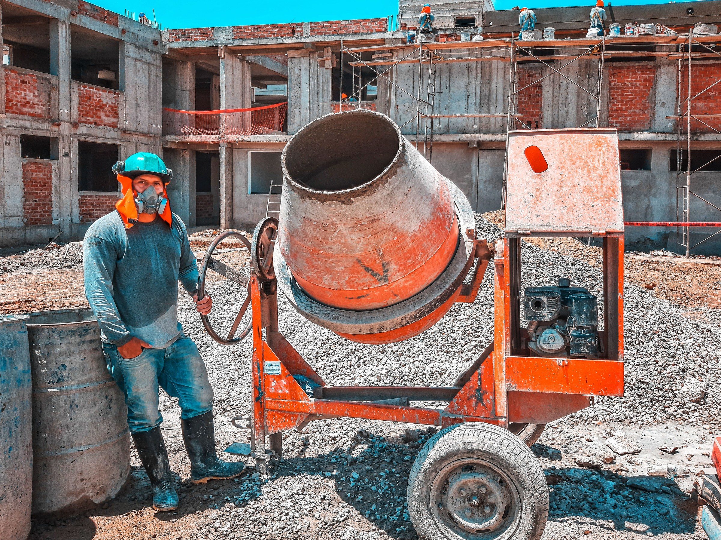 A construction worker operating a concrete mixer at an active building site, emphasizing safety gear