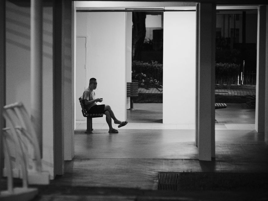 A man sitting alone on a bench in a quiet covered walkway, illustrating the work of a bail lawyer in Dubai