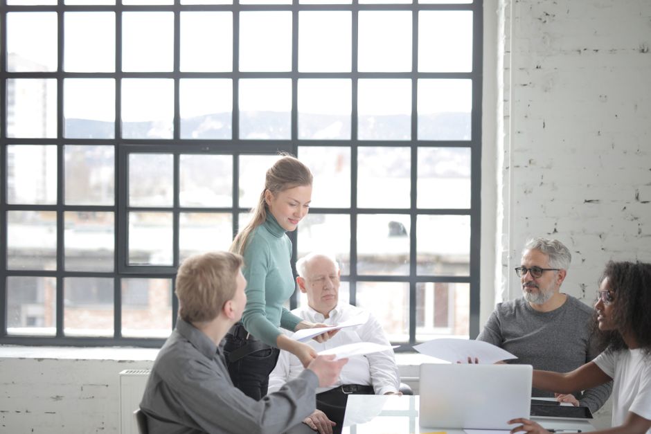 Colleagues around a meeting table passing printed documents between them, illustrating employment law in Dubai on termination