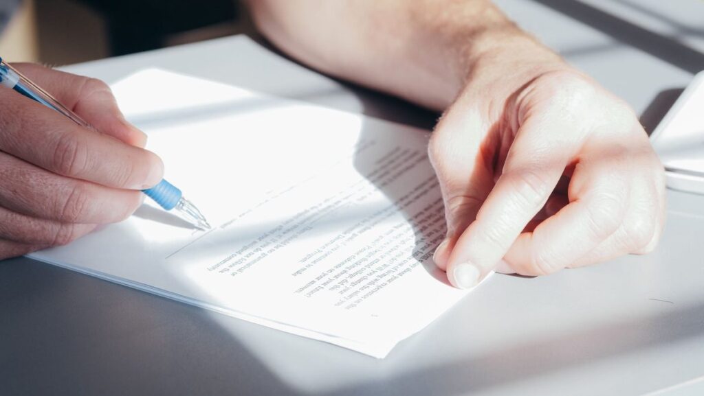 Close view of hands signing a paper with a blue pen on a desk