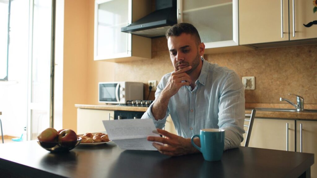 Man at a kitchen table reading a letter and thinking about the UAE attorney general summons