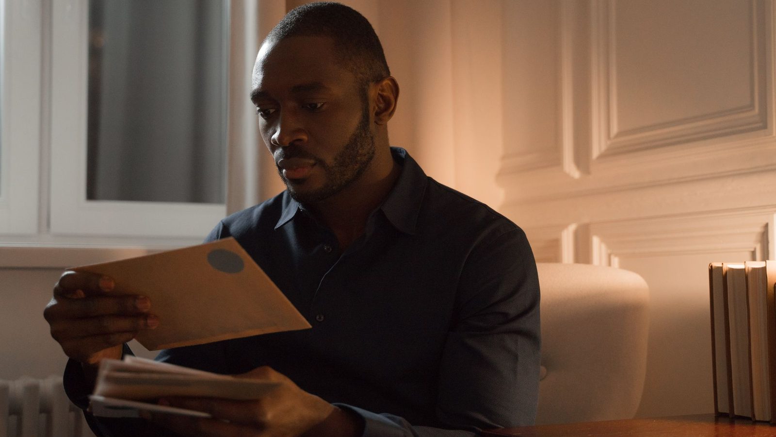 Man sitting at home in a warmly lit room reading a letter from an envelope