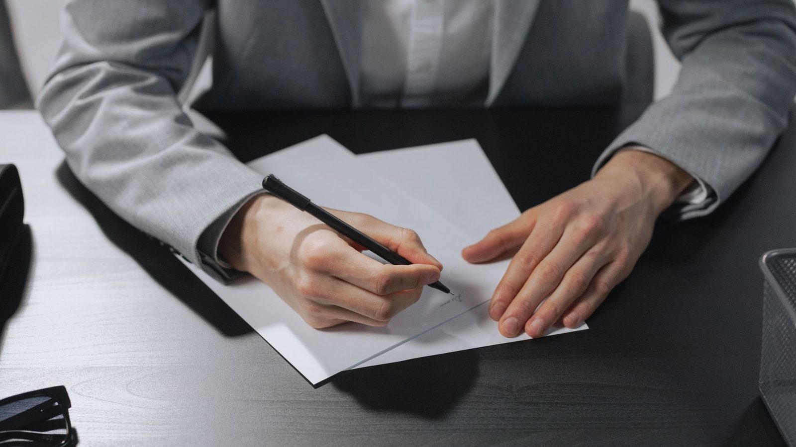 Hands holding a pen over a document on a dark office desk before signing